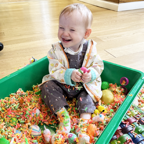 Little girl looking excited in a ball pit with lots of colourful confetti around her.