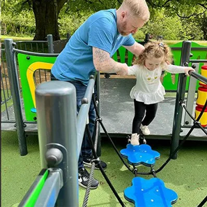 Father helping his daughter walk across blue flower pads outside the alan shearer centre